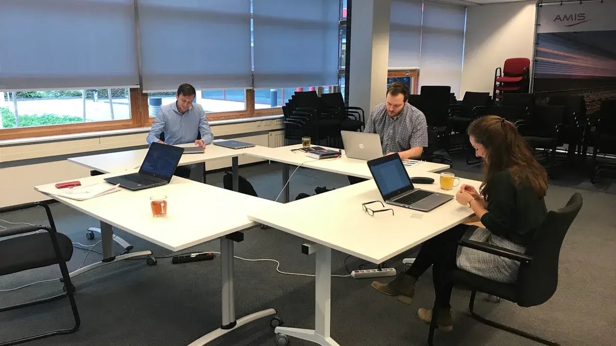 Collega's zitten tegenover elkaar aan tafel met hun laptop