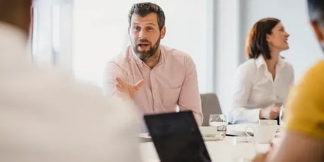 Consultant in roze blouse die aan vergadertafel iets uitlegt