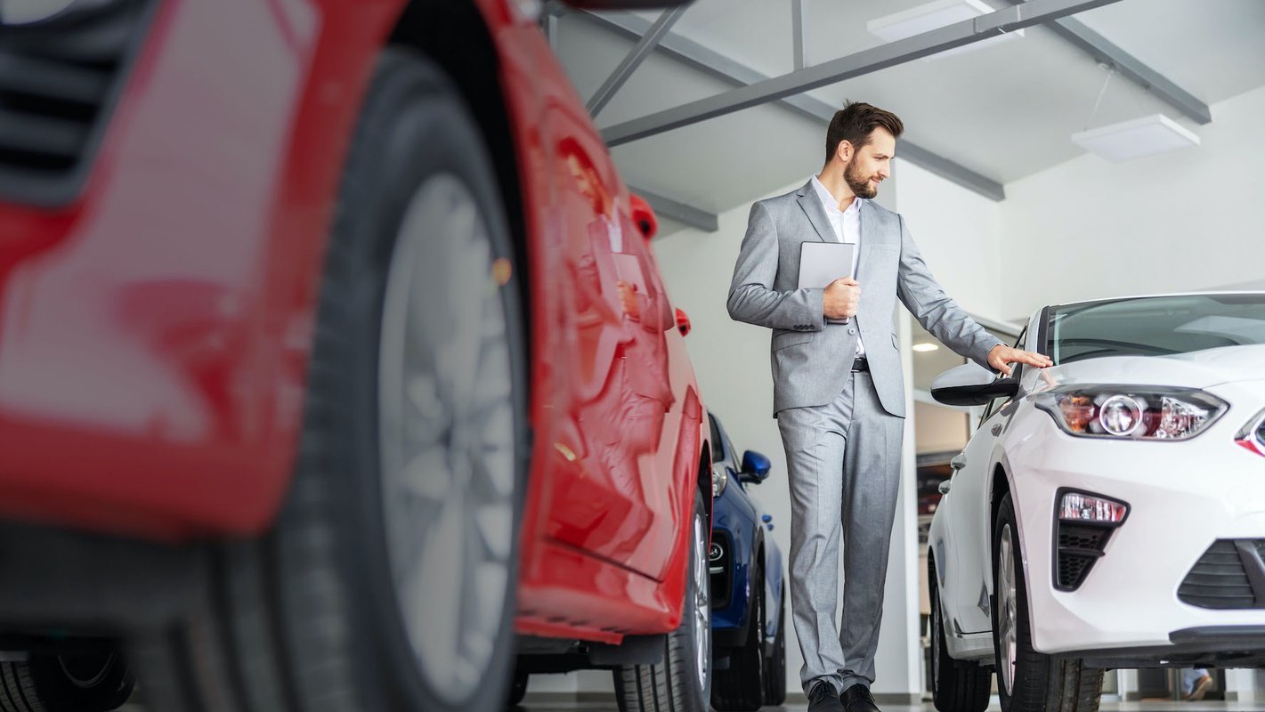 Man in grijs pak loopt tussen de showroom auto's