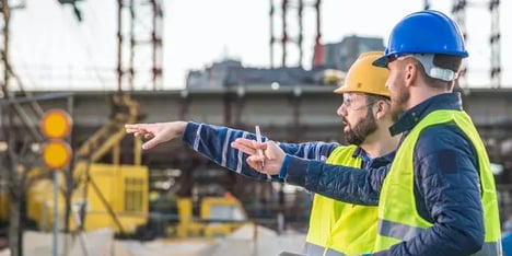 Twee mannen met helm en veiligheidshesje op de bouwplaats die wijzen