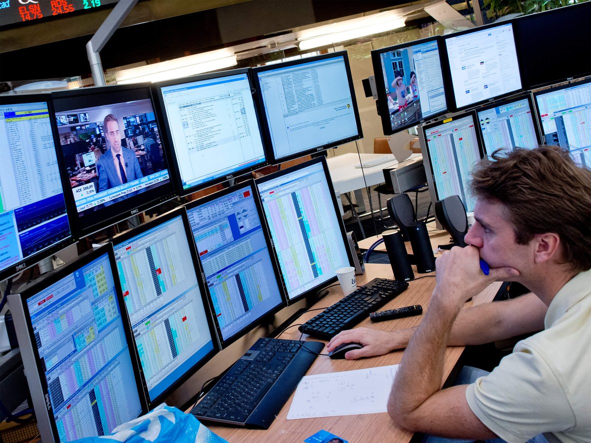 man kijkt serieus naar meerdere computerschermen voor hem