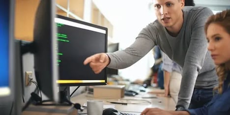 twee collega's voor een computer scherm, man wijst wat aan