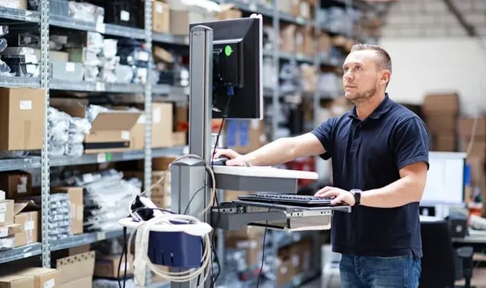 Man staand achter computer in een magazijn 