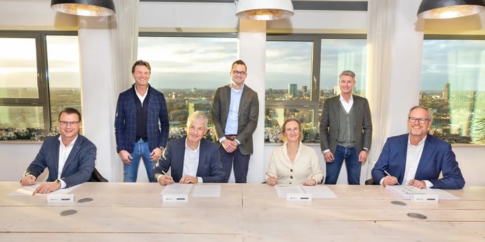 drie mannen en een vrouw aan tafel die overeenkomst tekenen en drie mannen die achter ze staan