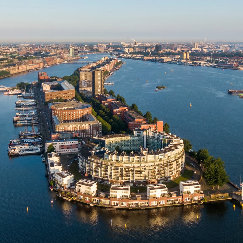 Aerial photo of a residential area by the water in Amsterdam, featuring modern buildings and boats along the quay.