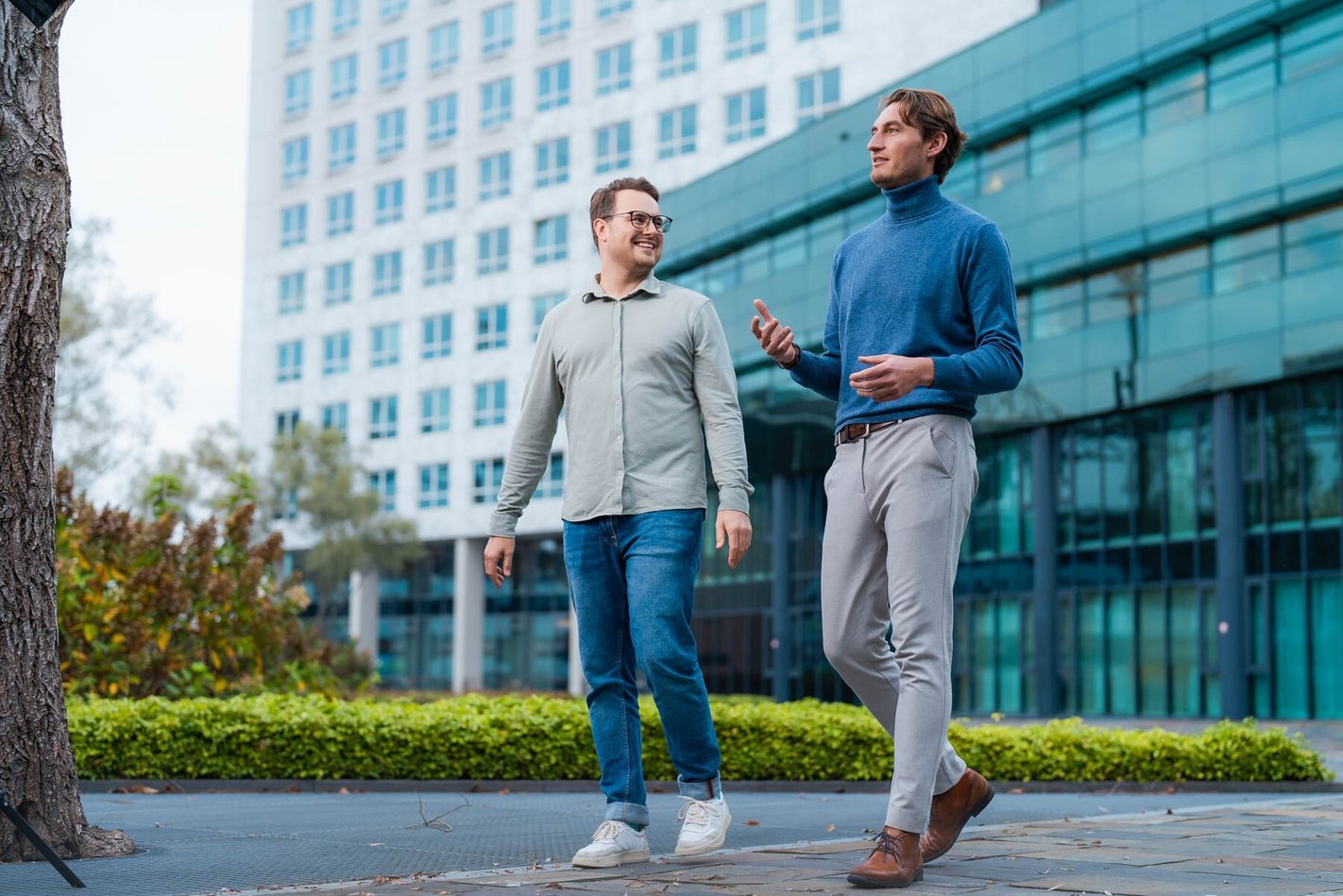 Dois homens estão a caminhar fora de um escritório, conversando um com o outro.