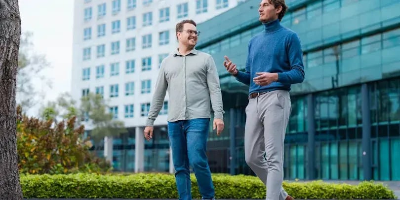 Dois homens estão a caminhar fora de um escritório, conversando um com o outro.