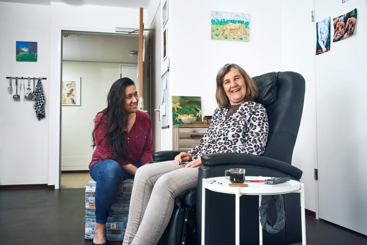 Lachende oudere mevrouw in een woonlocatie met een lachende medewerkster naast zich