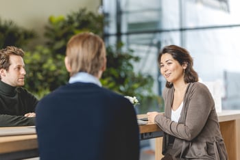 Drie collega’s in gesprek aan een tafel in een moderne kantooromgeving.