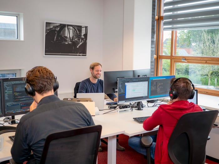 Drie mensen werken samen aan computers in een modern kantoor.