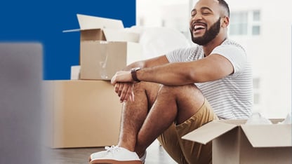 man zit lachend op de vloer tussen open verhuisdozen