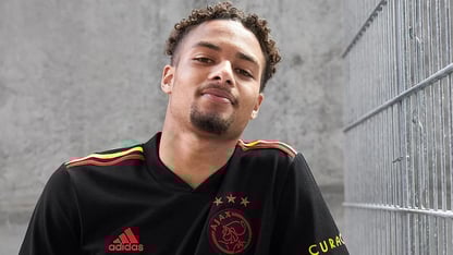 jonge man in zwart voetbalshirt van Ajax leunend tegen een betonnen muur en metalen hekwerk