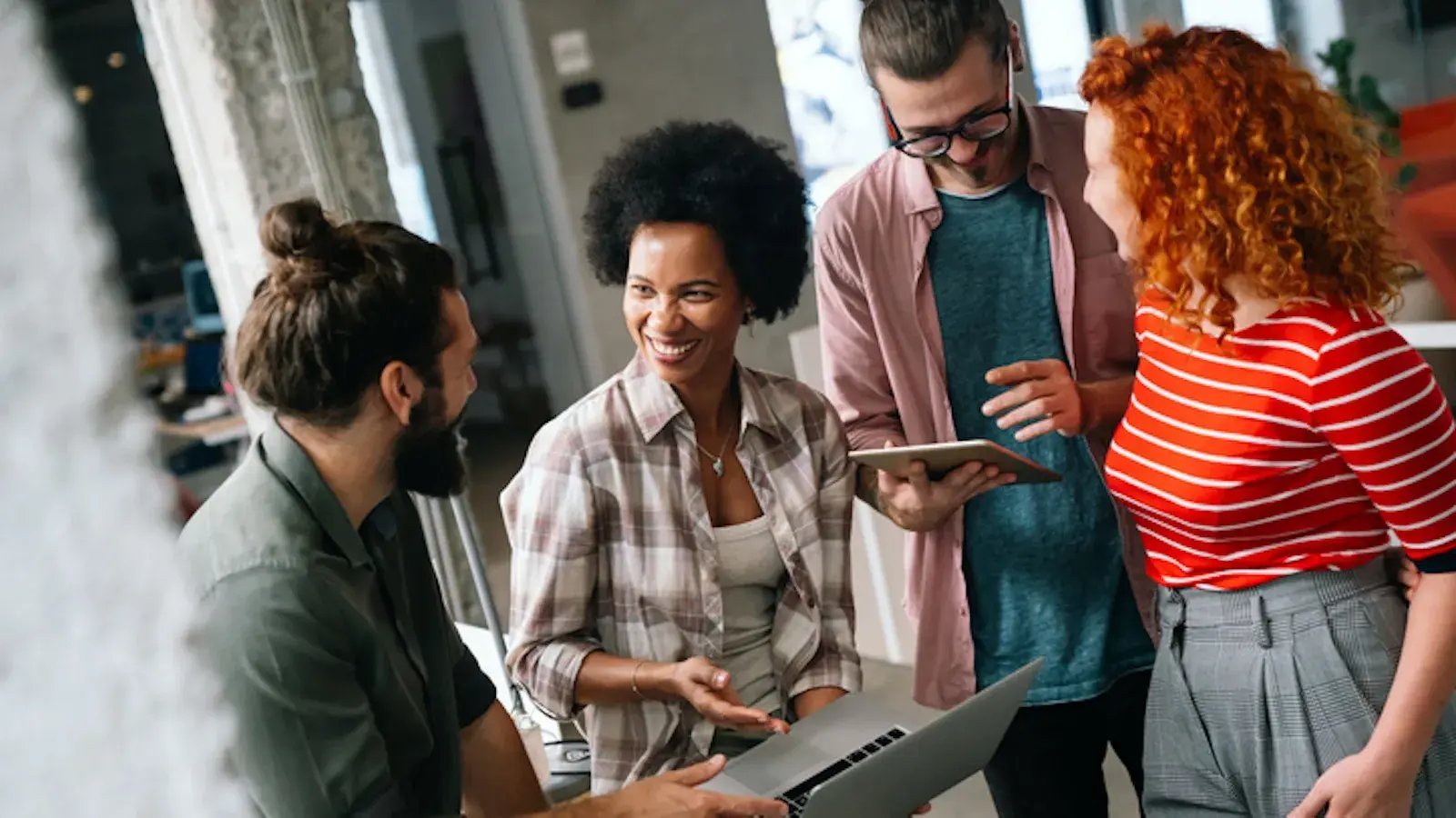 A female colleague is smiling at her male colleague while in a group.