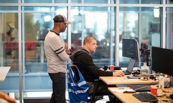 A male colleague is looking over another colleague's shoulder at the computer.