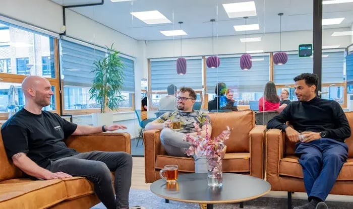 A group of colleagues is sitting on chairs, having tea together.