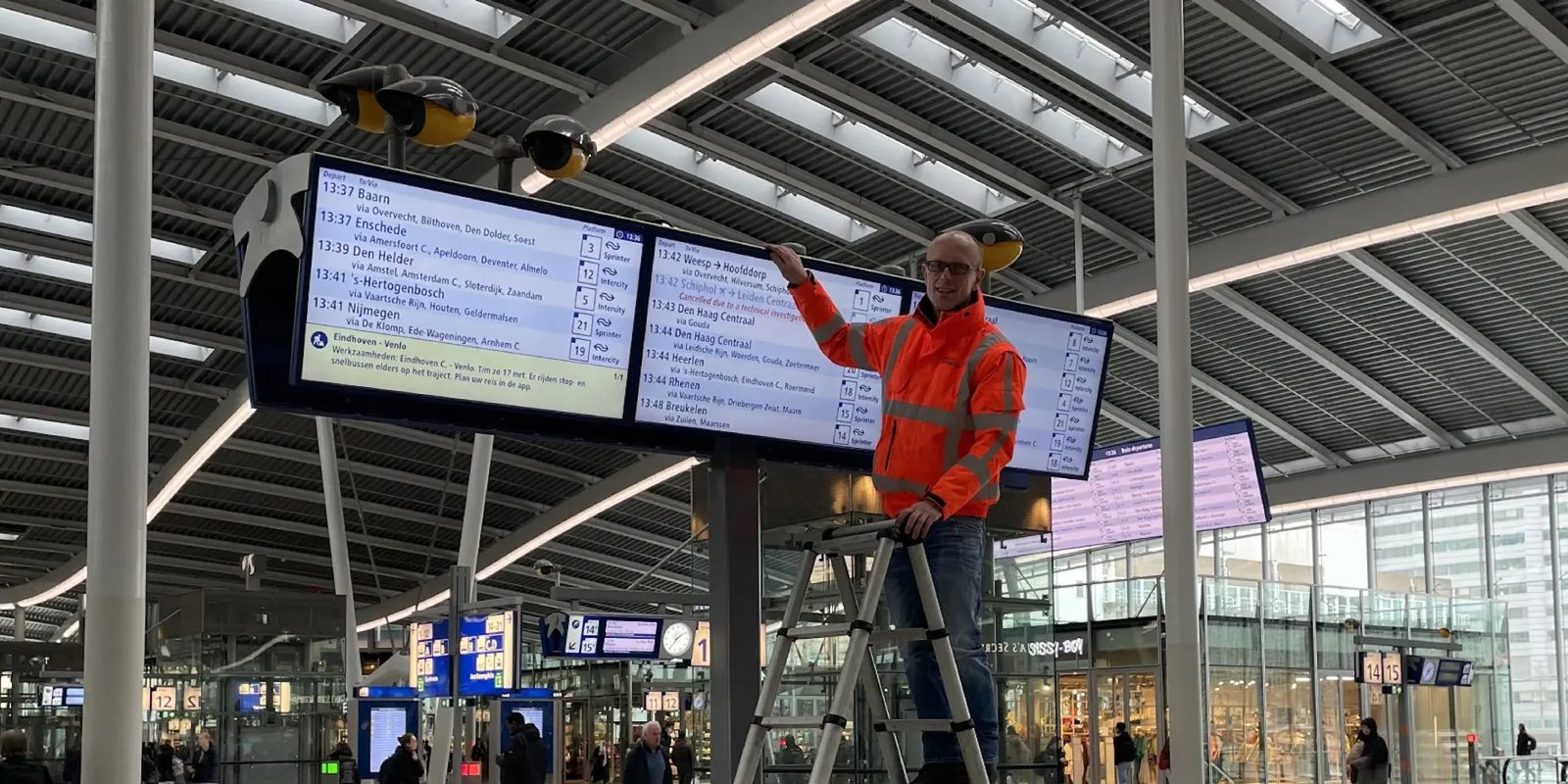 man op een ladder bij de digitale borden van NS