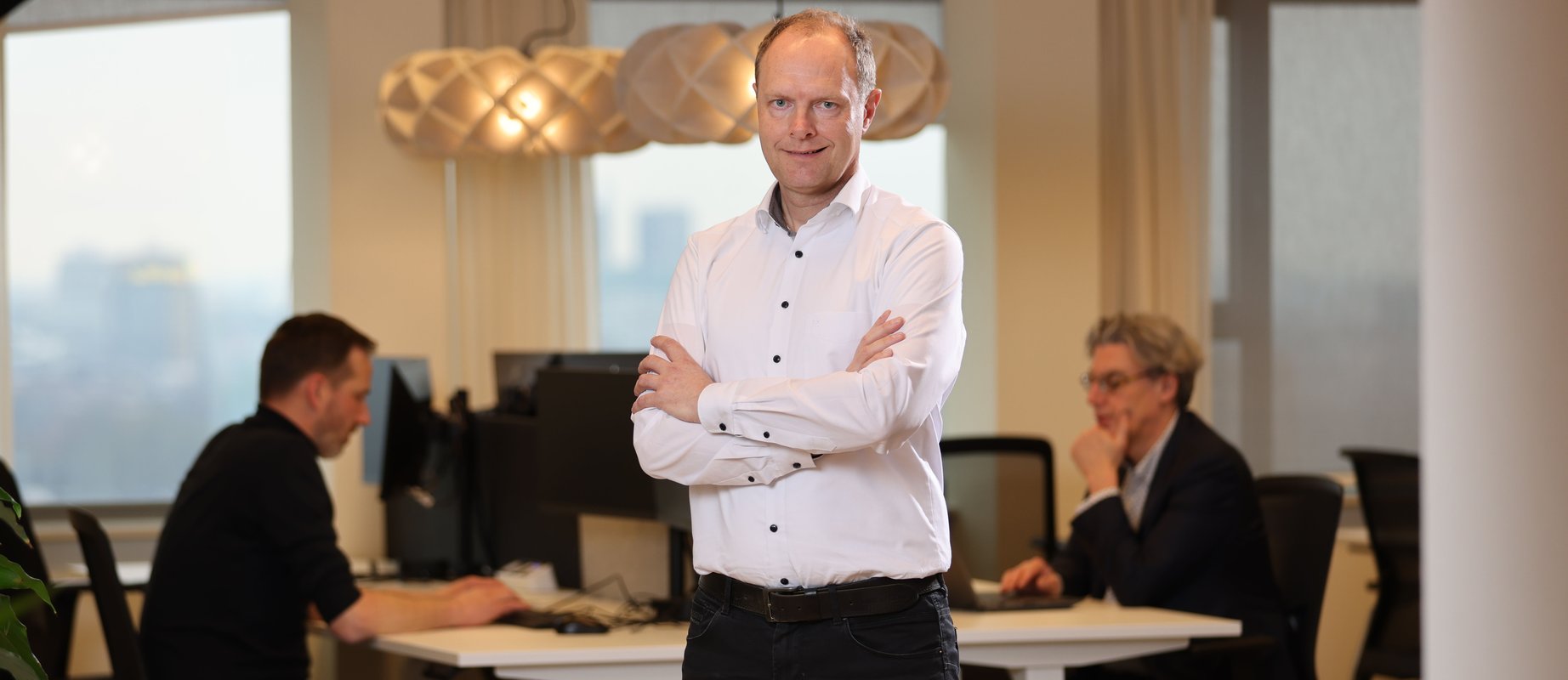 robert standing in an office where two of his colleagues are working hard behind him