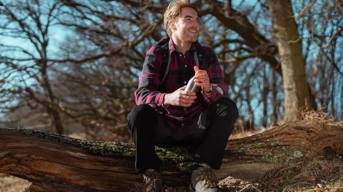 Jonge man zit op een boomstam en kijkt lachend naar rechts.