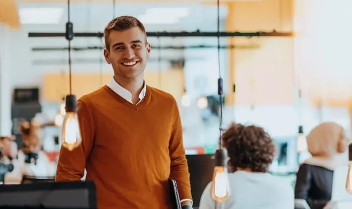 Mannelijke collega in oranje trui lacht vriendelijk.