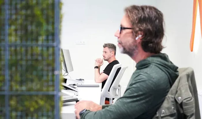 Two men are sitting behind their desks and concentrating on their desktops.