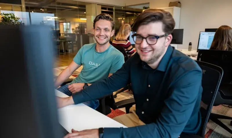 Twee jonge, mannelijke medewerkers die samen naar een computerscherm kijken