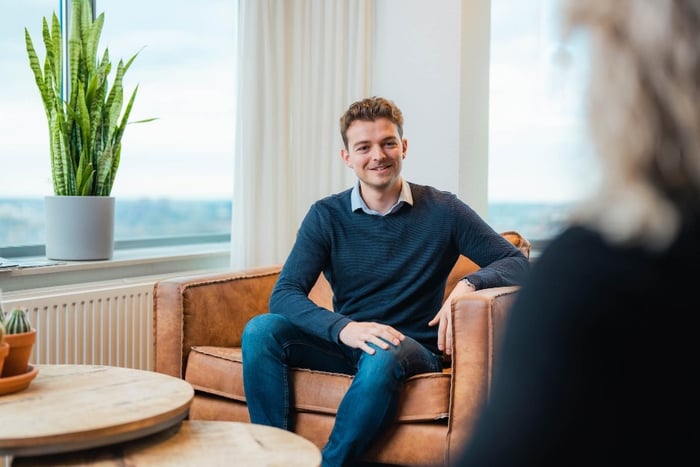 Cas zit op een bruine leren stoel en lacht