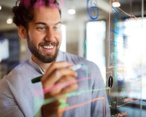 Jonge man schrijft met gekleurde stiften op een glazen wand
