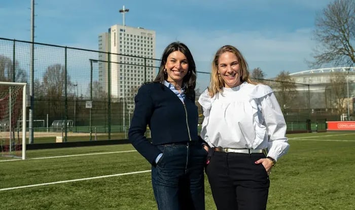 Twee vrouwen lachend naar de camera op een voetbal veld