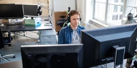 Man met koptelefoon op kantoor voor twee beeldschermen een het werk