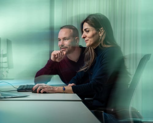 Mannelijke en vrouwelijke collega kijken naar computers.