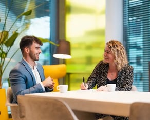 Twee collega's overleggen met een kop koffie.