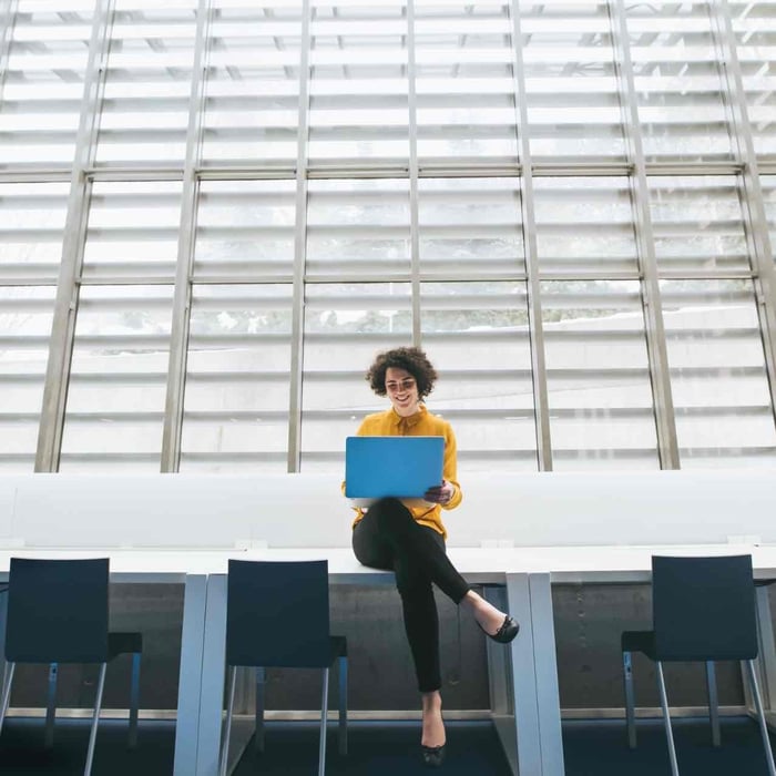 Vrouw zit op bureau met laptop op haar schoot.