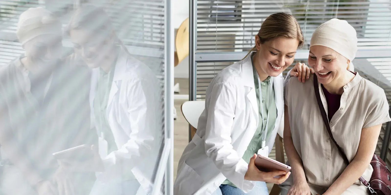 Een zieke vrouw met verband om haar hoofd en haar verpleegster lachen naar een tablet.