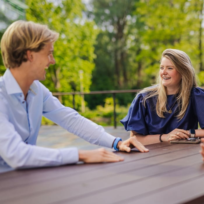 Collega's lachend naar elkaar buiten op een bankje. 