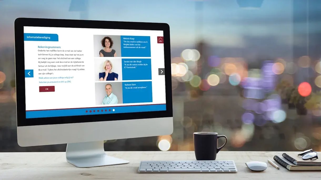 Een tafel met een computer scherm, koffiebeker, boeken, en een bril