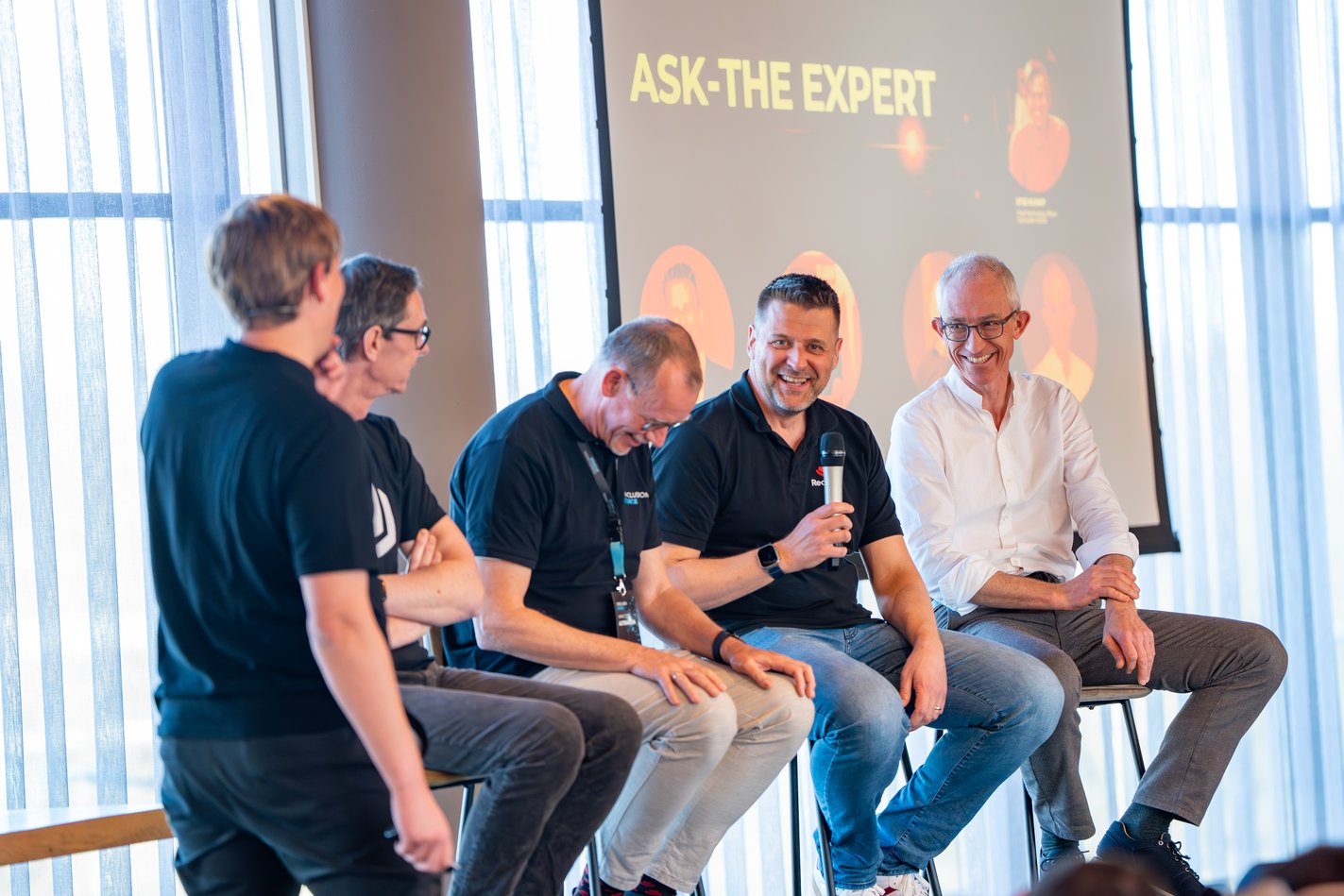 Event met meerdere mannelijke sprekers op het podium met microfoon.