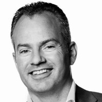 Dit is een zwart-wit portret van een man met kort haar, een glimlach, en een nette uitstraling.