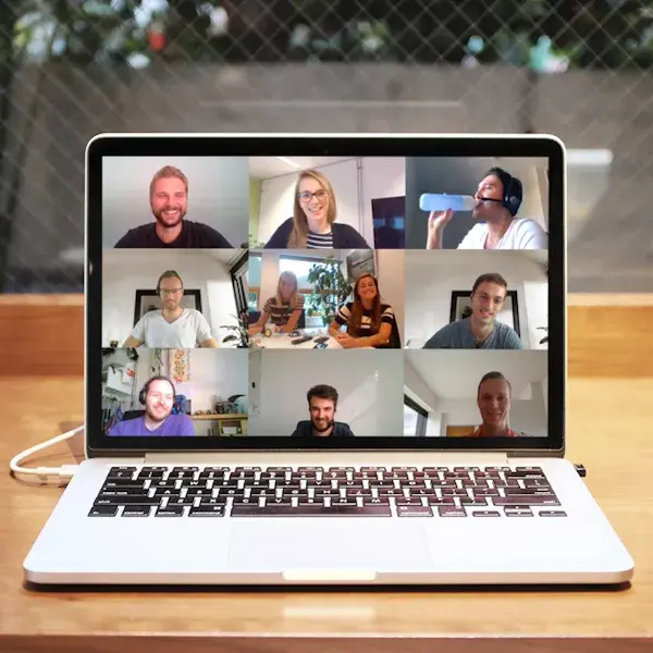Laptop op een tafel met een open videogesprek, waarop negen mensen in een rasterweergave zichtbaar zijn tijdens een online meeting.