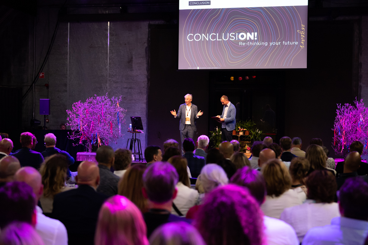 zaal binnen met twee mannen op podium voor publiek