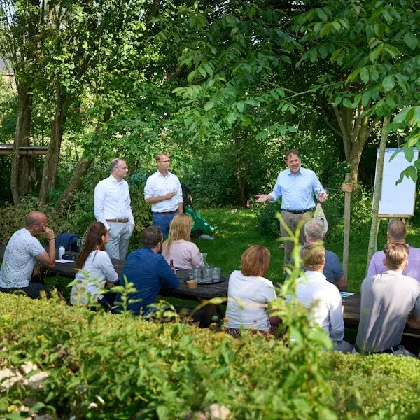 Groep mensen in zakelijke kleding die in een groene tuin presentatie bijwonen