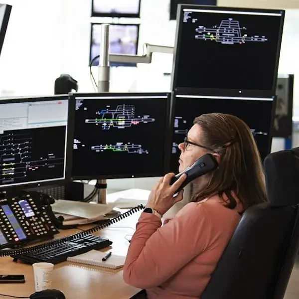mevrouw aan de telefoon met meerdere laptop schermen met technische info voor zich