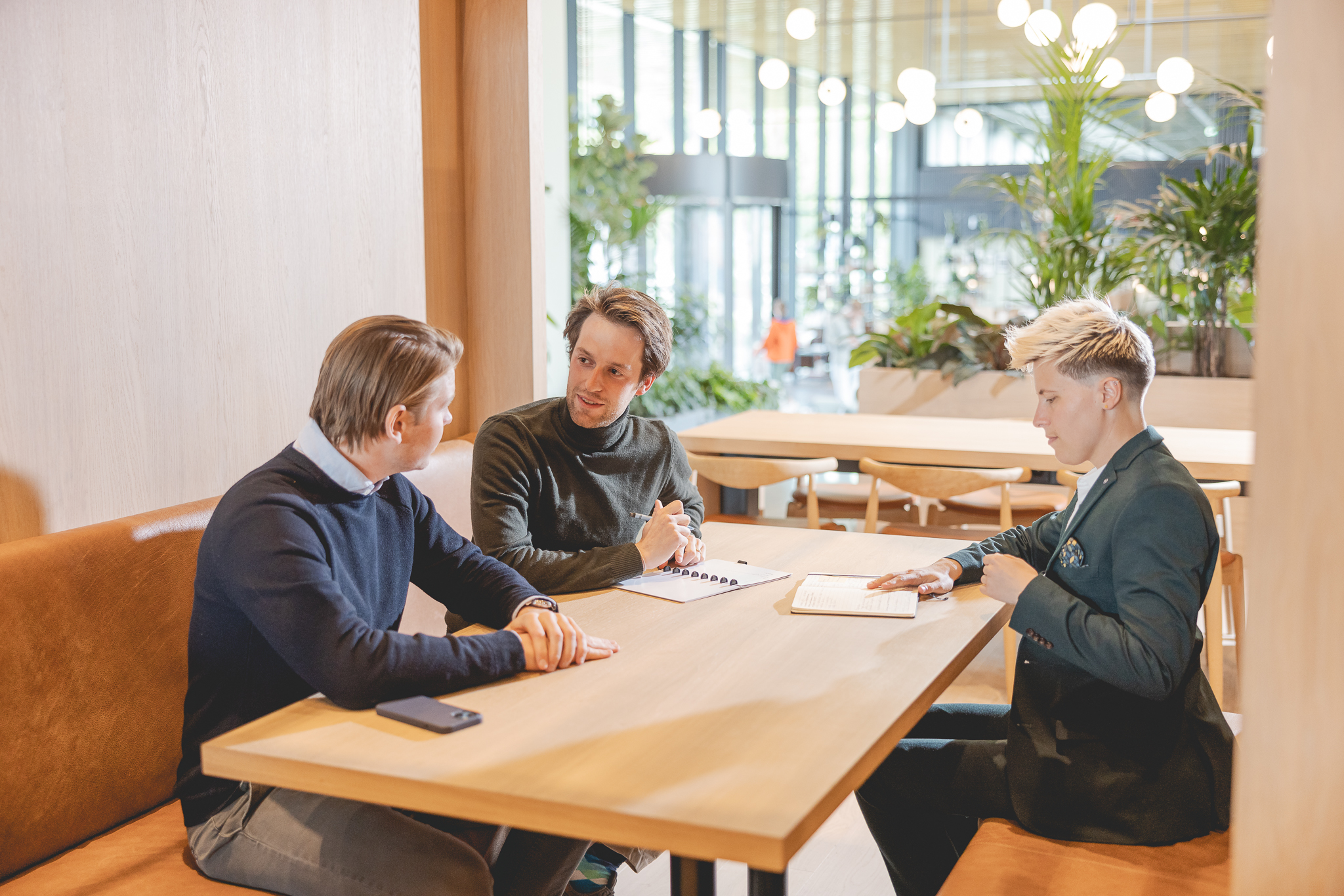 Drie collega's zitten aan een tafel met hun notitieboekjes en overleggen.