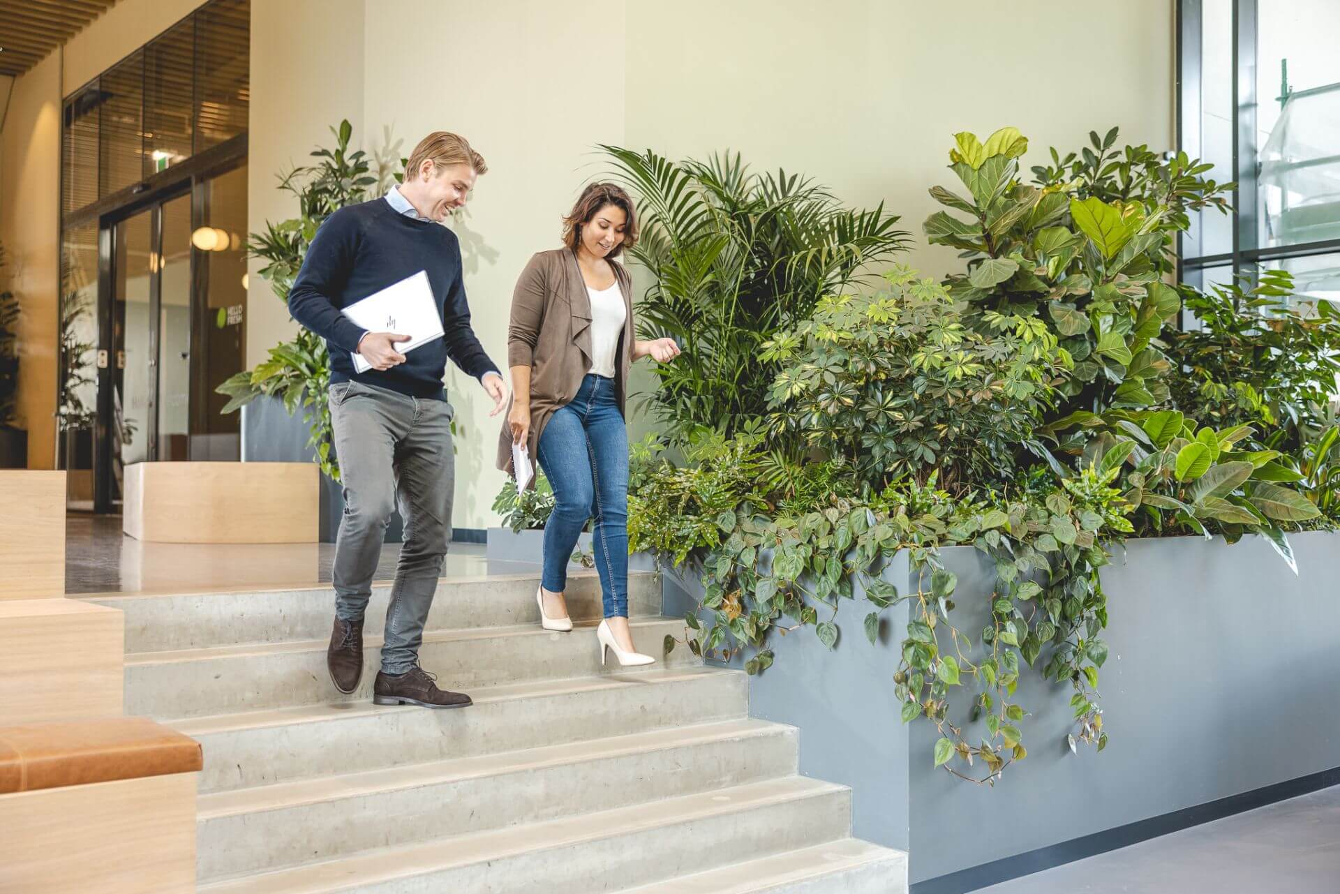 Twee collega's lopen met laptops in de hand de trap af.