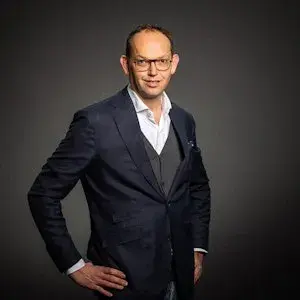 Zelfportrait van Robert Schras, een man in een donker pak met een bril en z'n handen in zijn zij