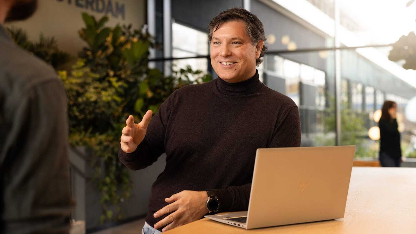Male colleague with a laptop holds out his hand to greet someone.