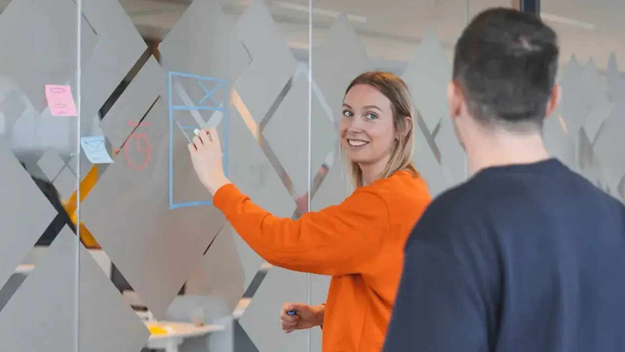 Vrouwelijke collega plakt post-its op een glazend wand.