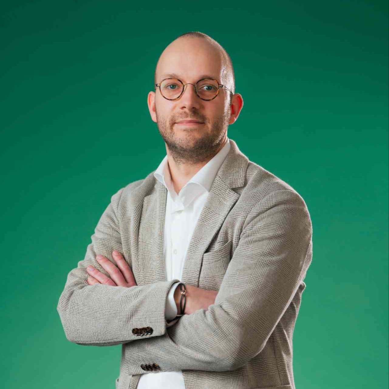 Mannelijke collega met armen over elkaar kijkt vriendelijk naar de camera.