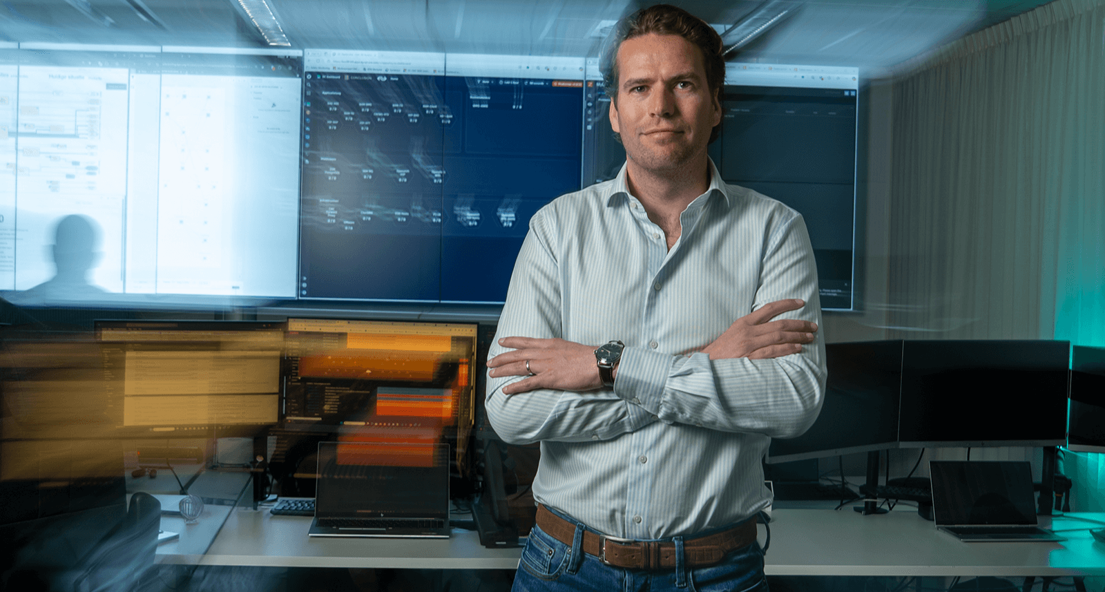Man crosses his arms and poses in front of his office desk.