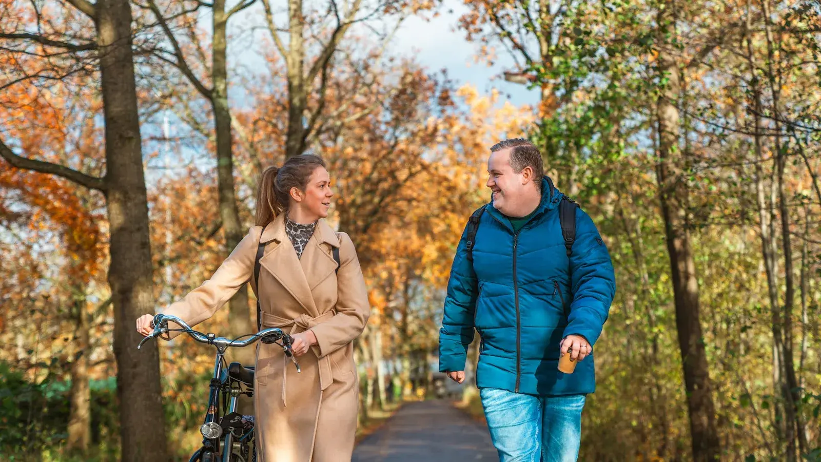 Vrouw loopt met de fiets aan de hand naast een man in een herfst bos