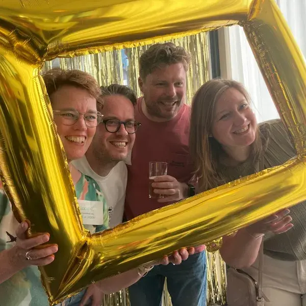 Vier voormalige collega's kijken door een fotoframe om samen op de foto te gaan